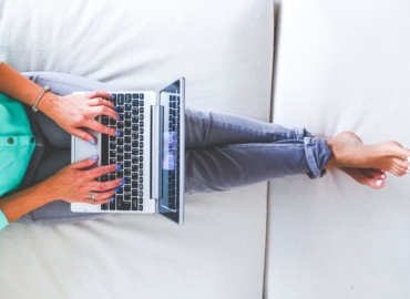 Home Office: Frau arbeitet mit Laptop auf dem Schoß auf dem Sofa